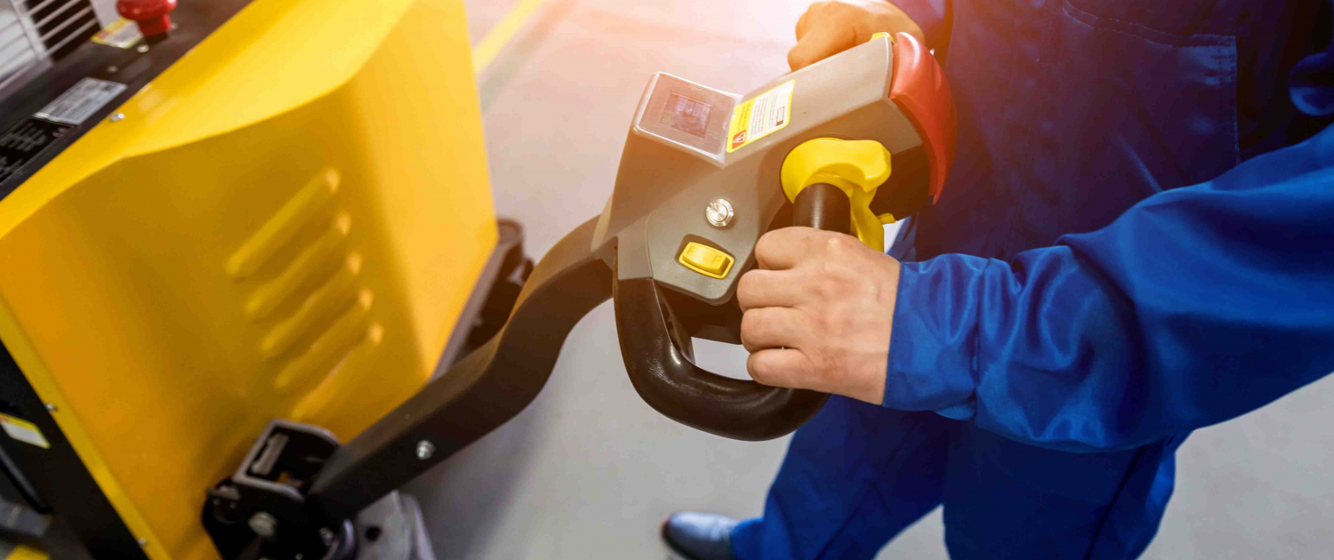 A worker in a warehouse uses a hand pallet stacker to transport pallets.